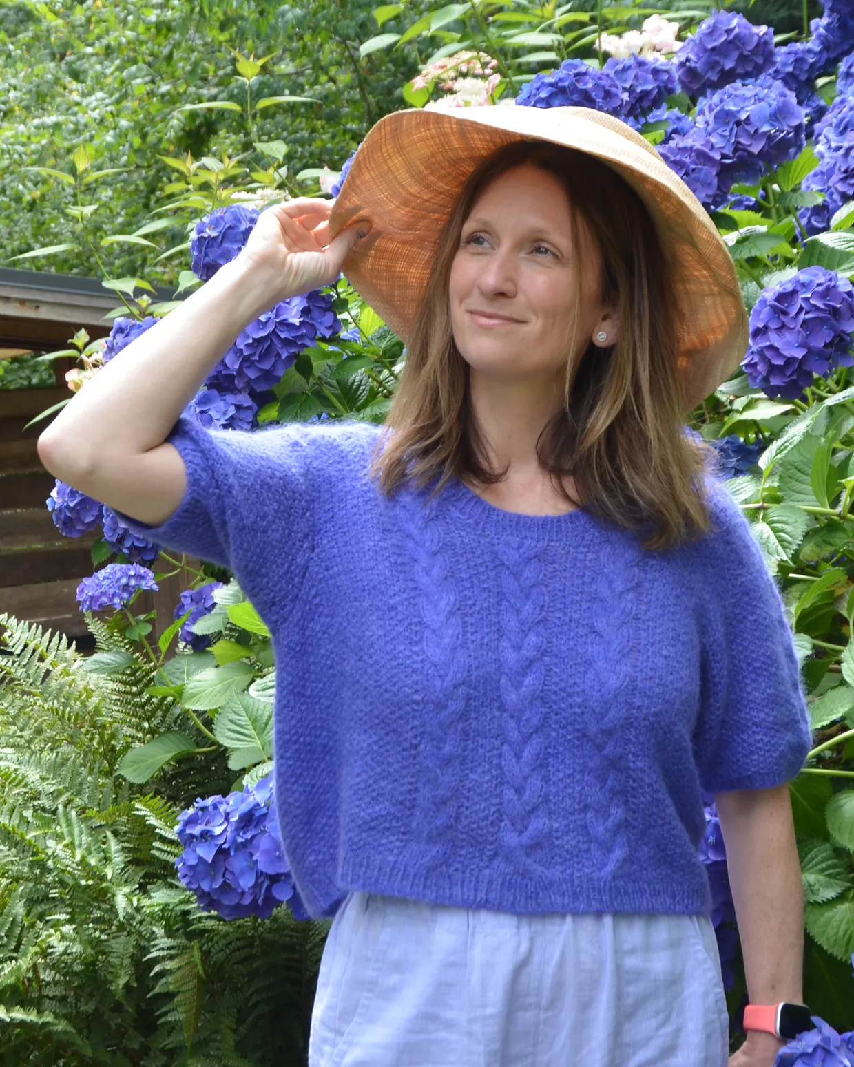 A woman wearing the Solstice Saddle pullover in a sunlit garden